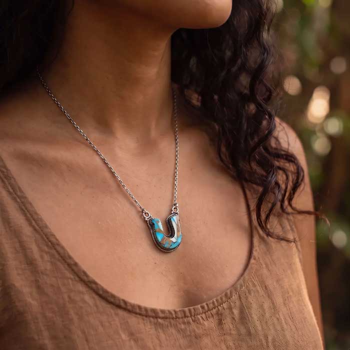 Kingman Turquoise Horseshoe Pendant Necklace set in sterling silver shown on neckline of horse lover. Turquoise shows richly colored matrix